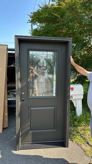 Black front door with glass panel, standing outdoors beside a truck and trees