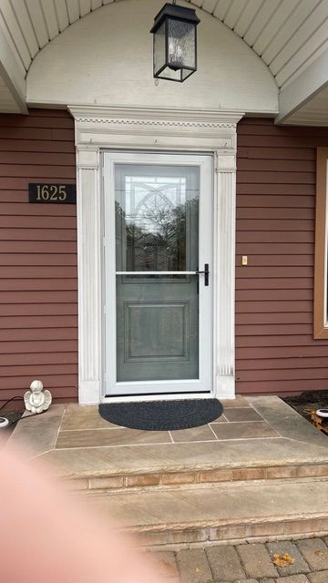 Front porch with gray door, white trim, red siding, small black mat, and hanging lantern light