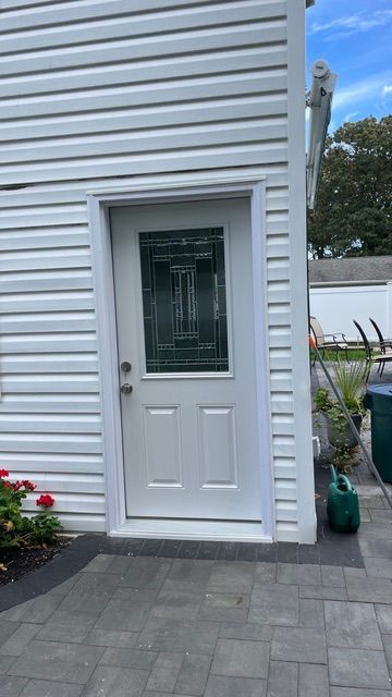 White exterior door with glass panel on a gray-sided house beside a paved patio.