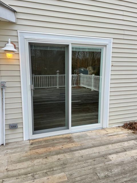 Sliding glass door on a beige-sided house, with a wooden deck and porch light beside it.