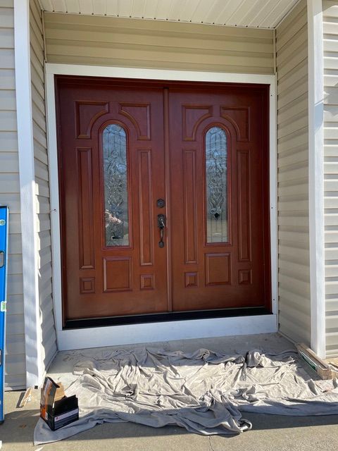 Front entry with double wooden doors and sidelights, a tarp spread across the porch for work.