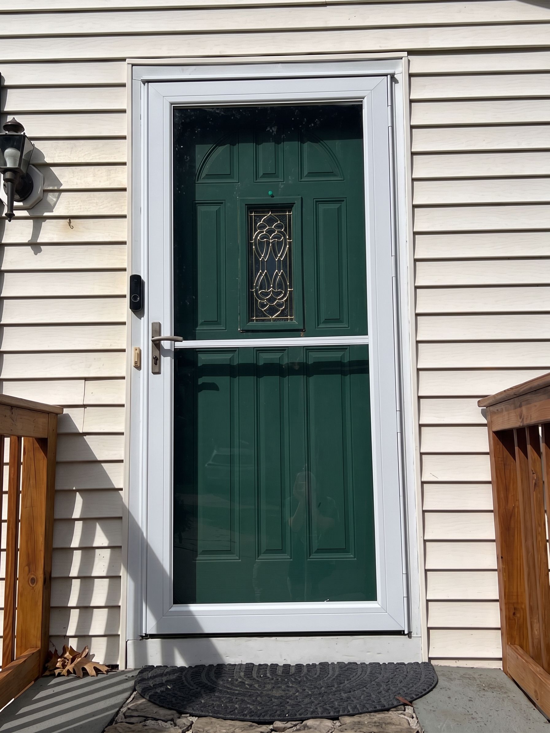 Green front door with small decorative window in a beige house exterior