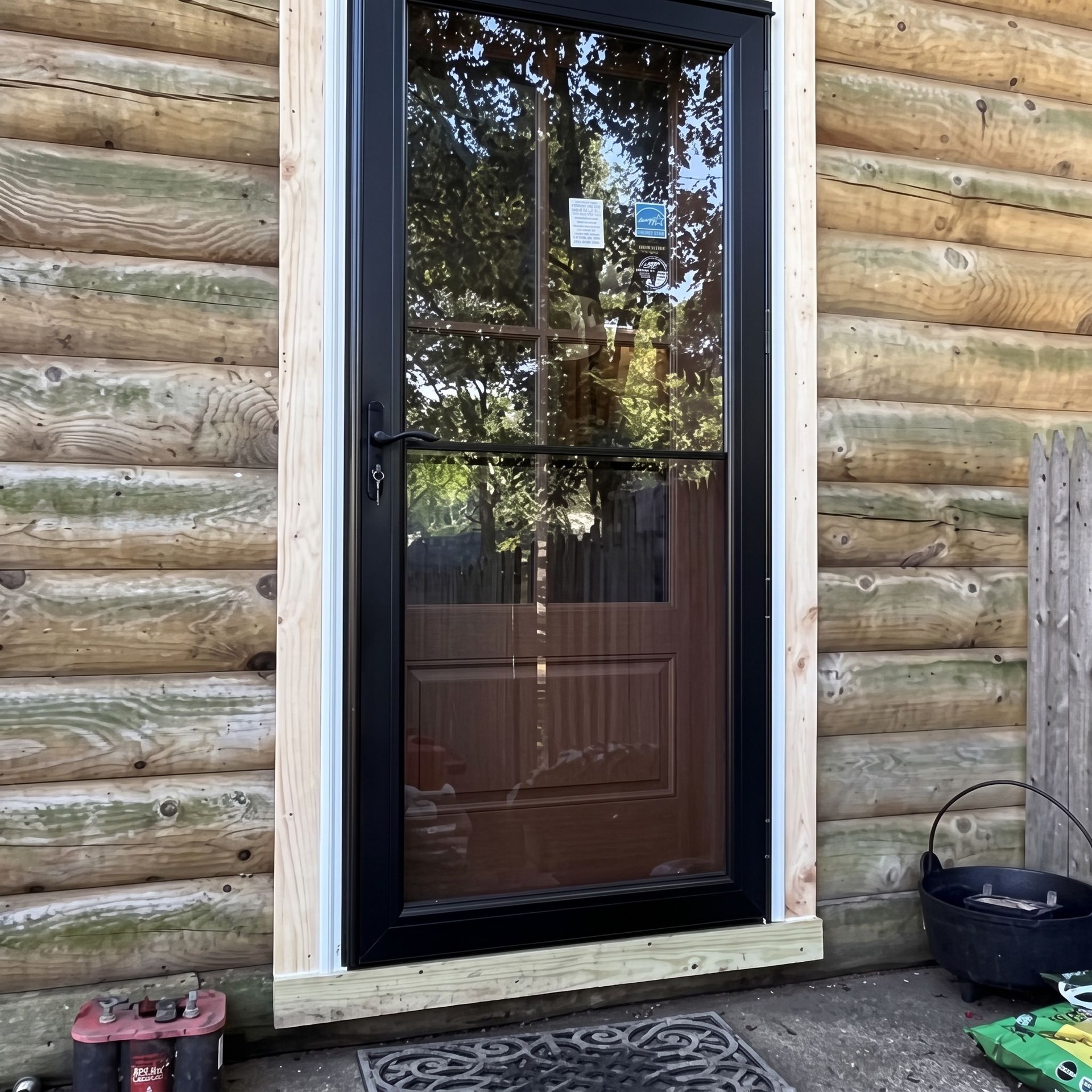Black screen door in a log cabin wall, with a step and bucket outside