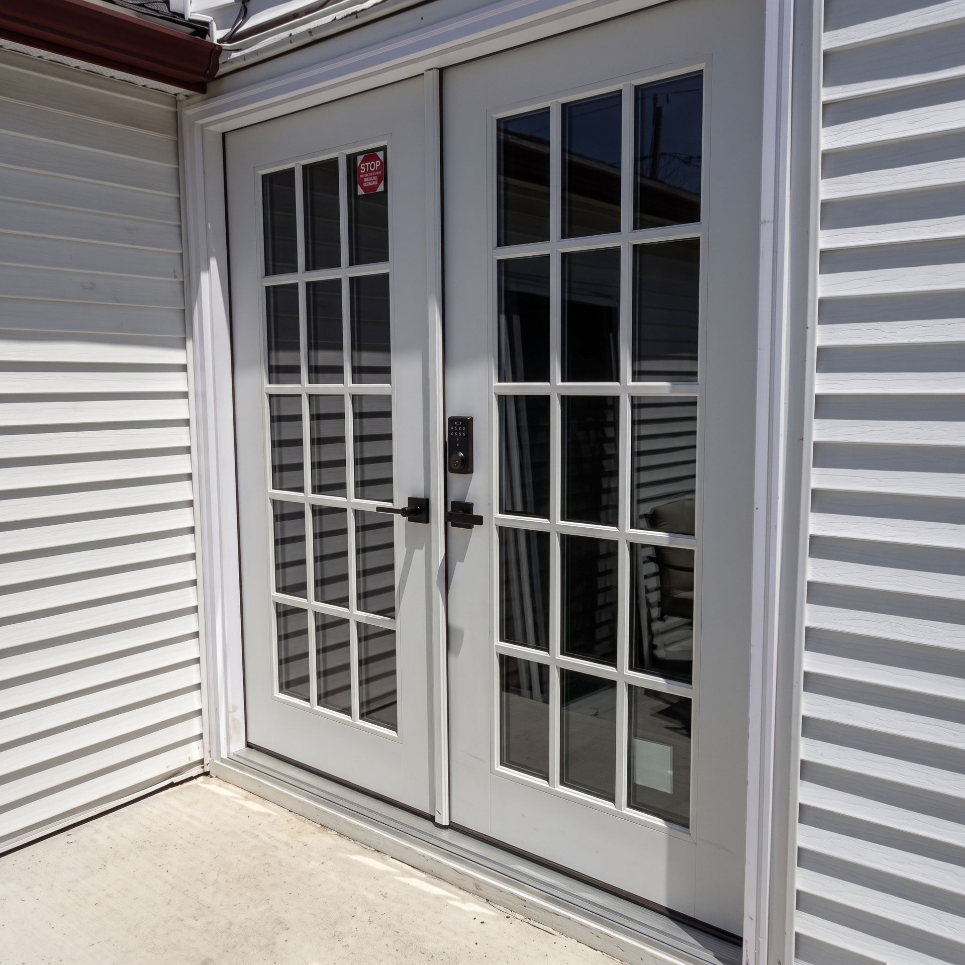 White French double doors with glass panes beside light gray siding and a concrete patio