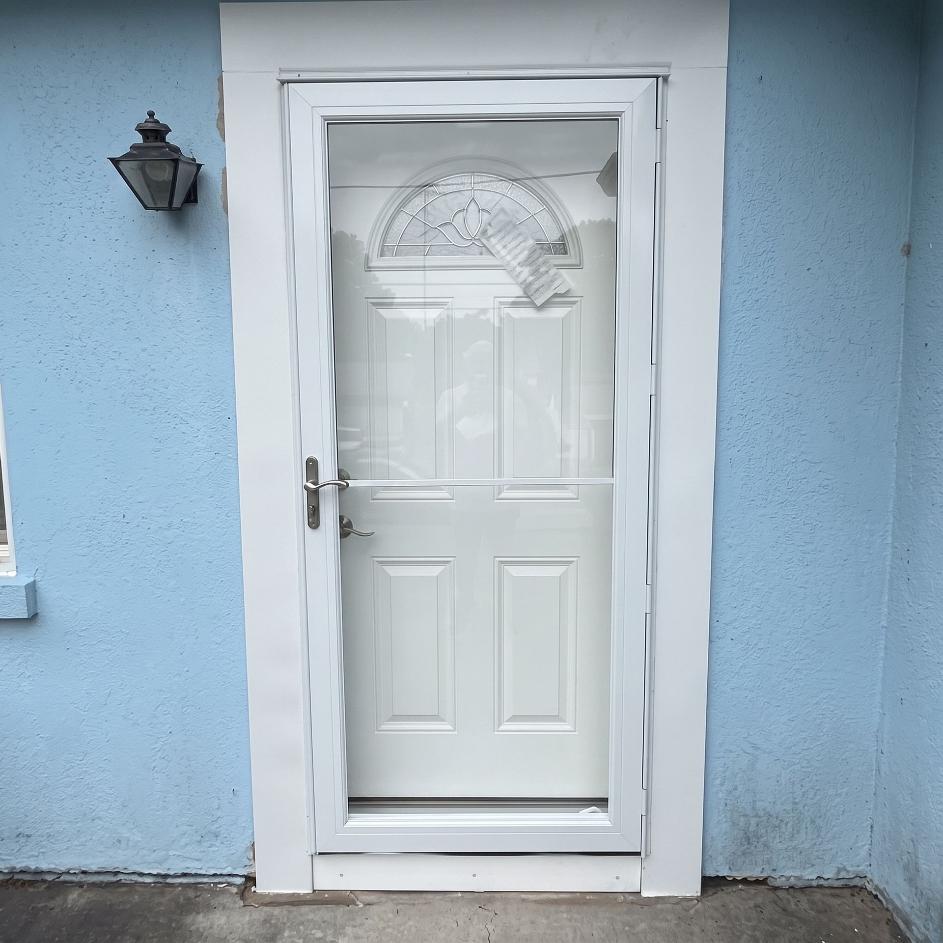 White front door with decorative glass panels set in a light blue exterior wall.