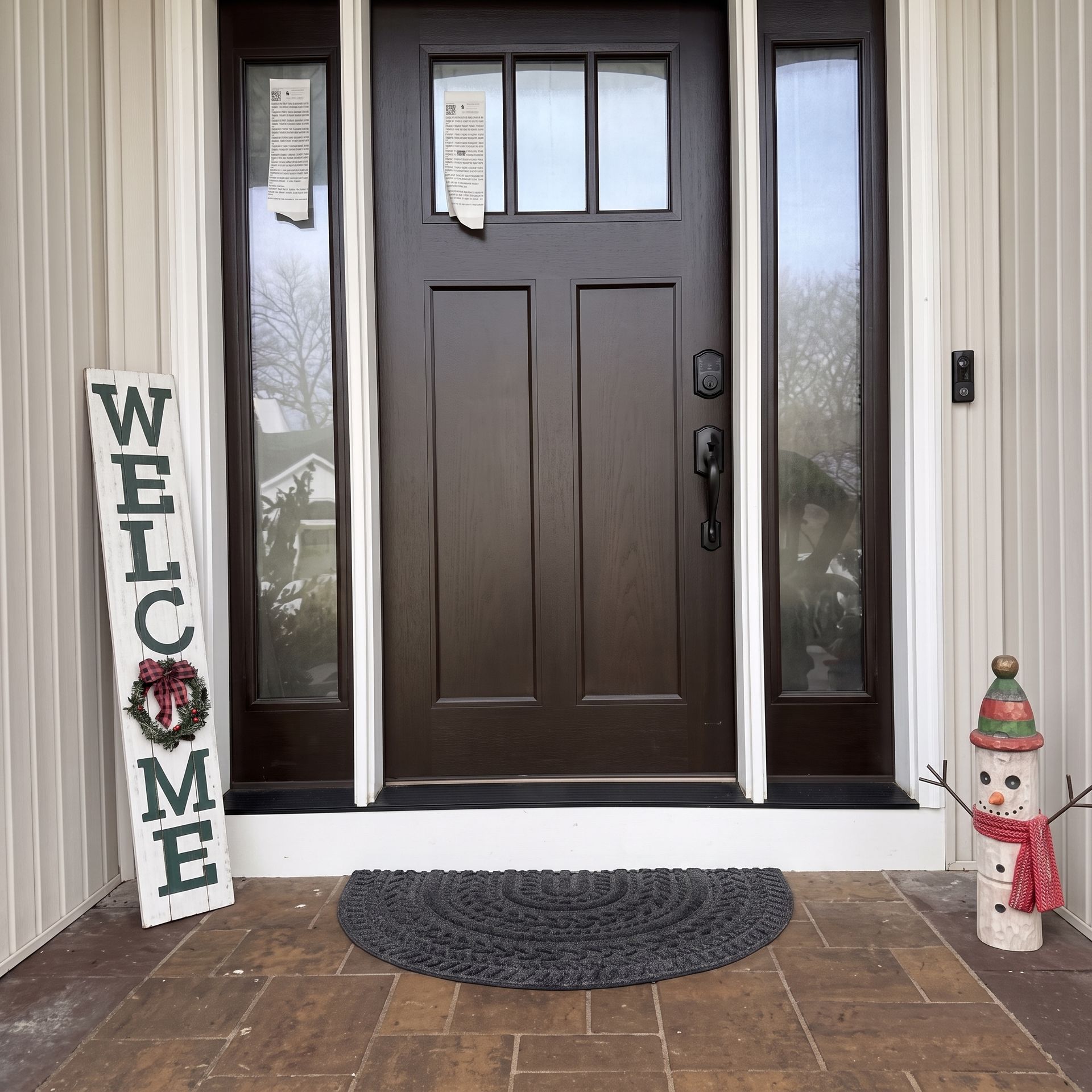 Front porch with dark brown front door, welcome sign, doormat, and small snowman decoration