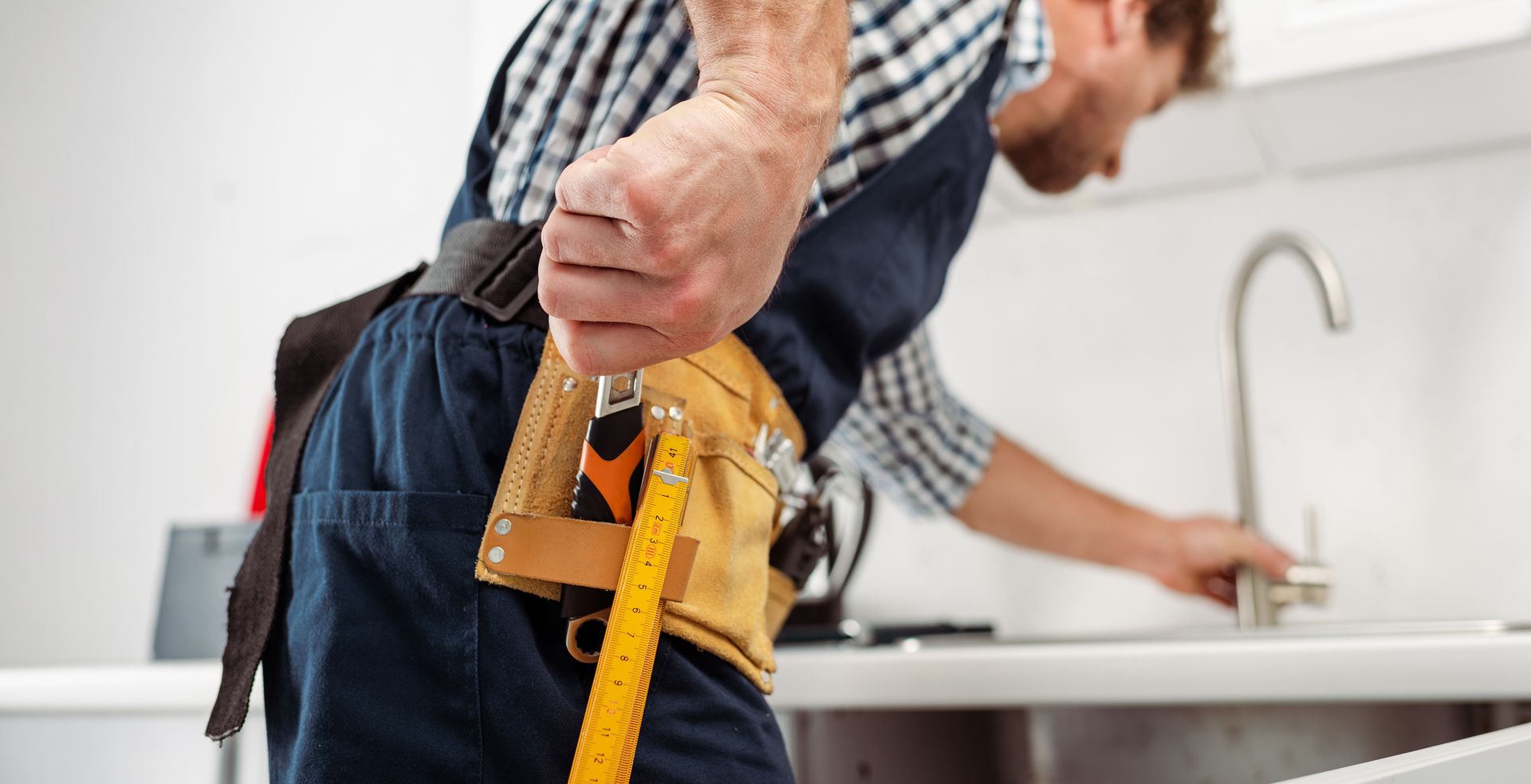 Worker using a tool belt fixing a sink in a kitchen