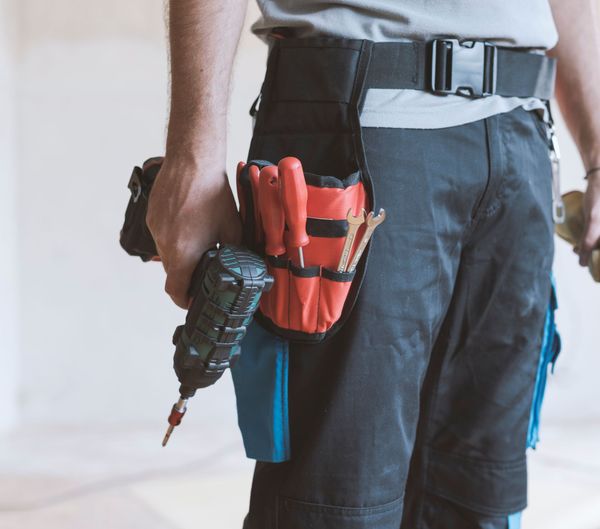Worker with tool belt holding a cordless drill and red screwdriver pouch