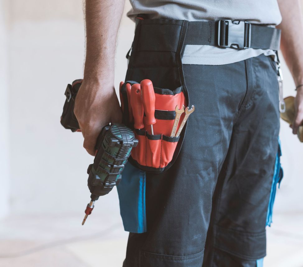 Worker with tool belt holding a cordless drill and red screwdriver pouch