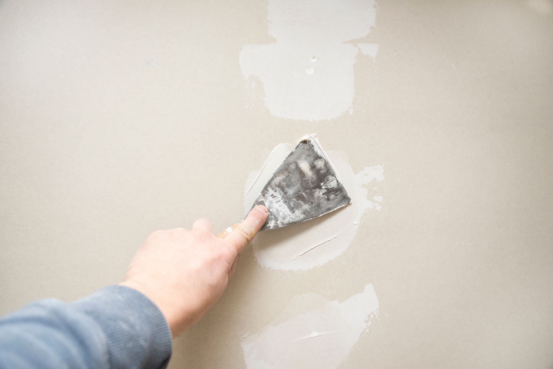 Hand using a putty knife to patch a beige wall with white spackle