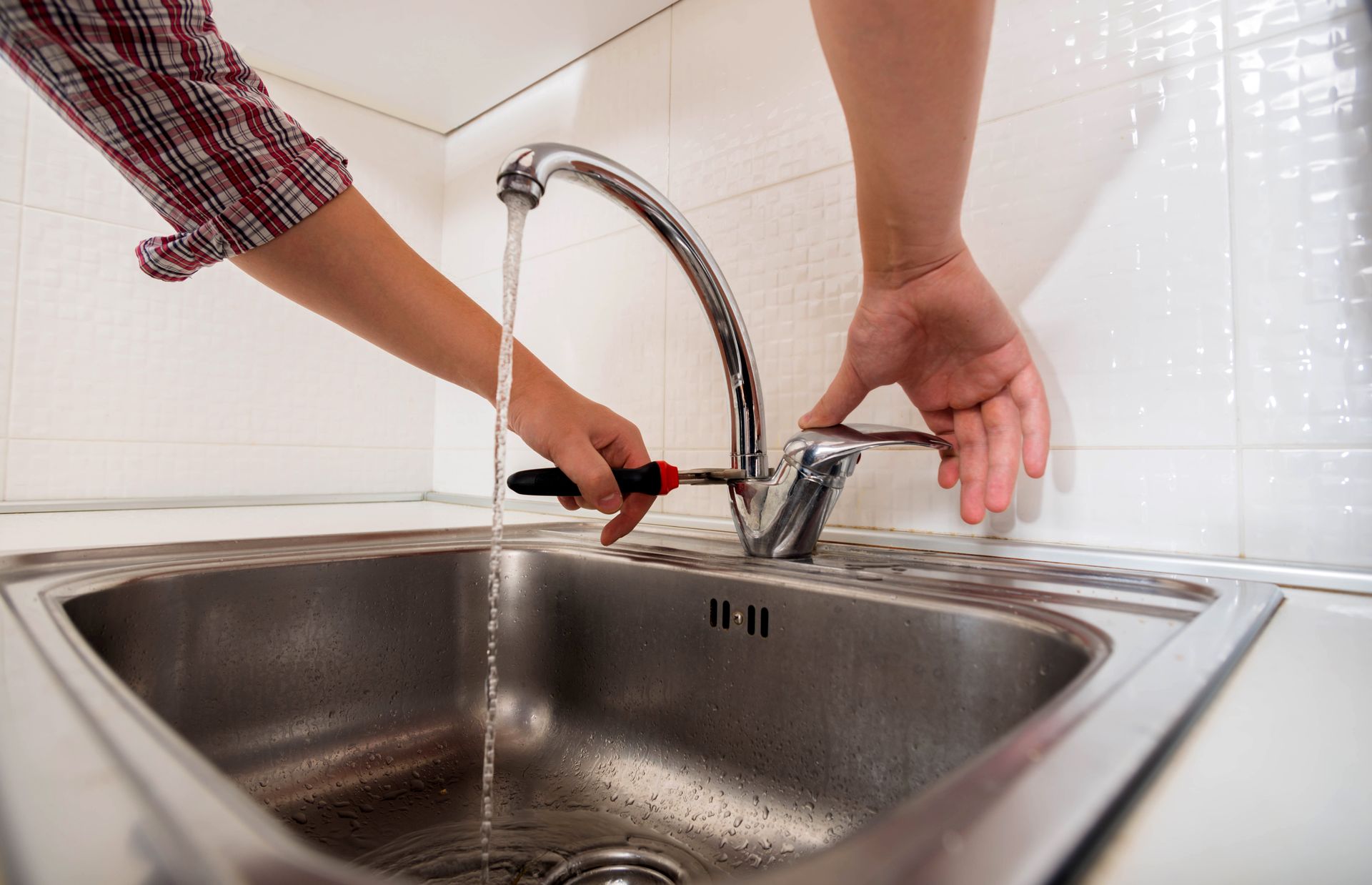 Hands using a wrench to install a kitchen faucet over a stainless steel sink