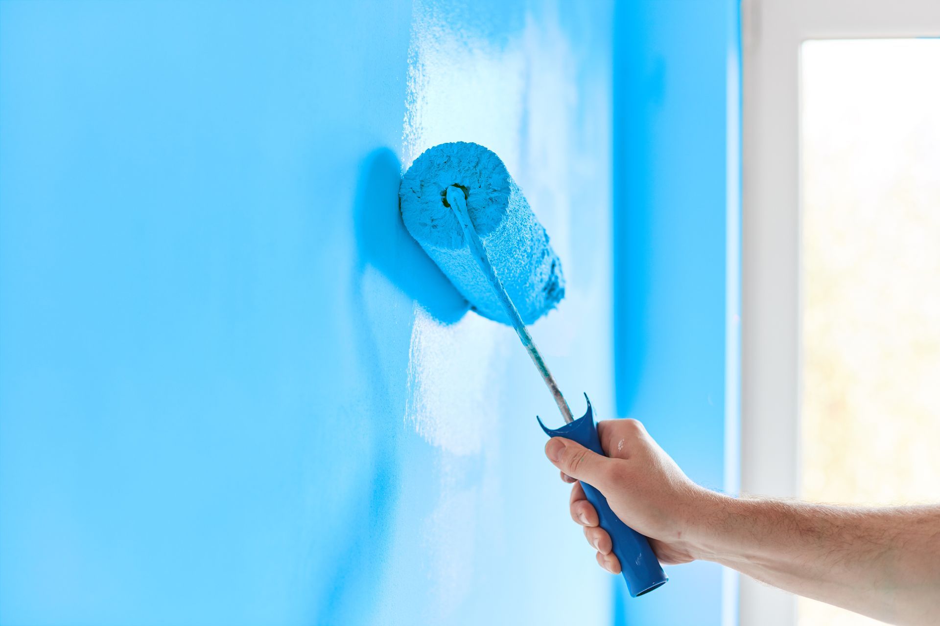 Hand painting a blue wall with a paint roller