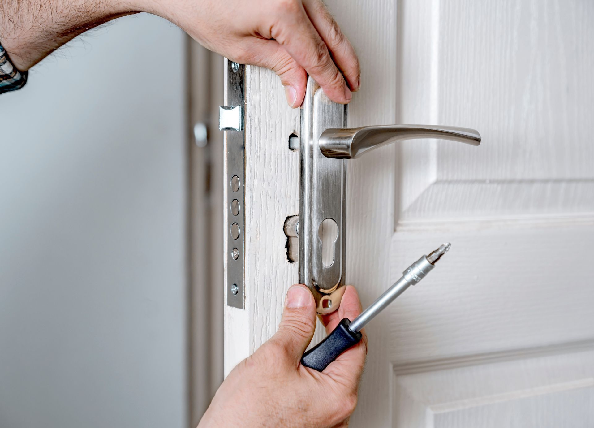 Hands unlocking a white door with a screwdriver and door handle visible