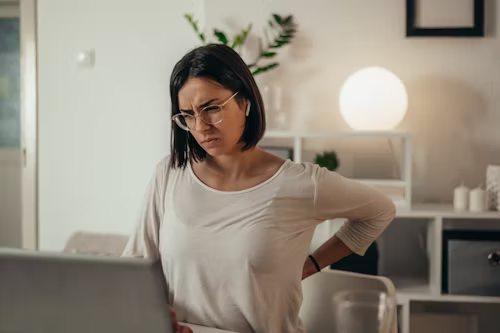 A woman is holding her back while using a laptop computer.