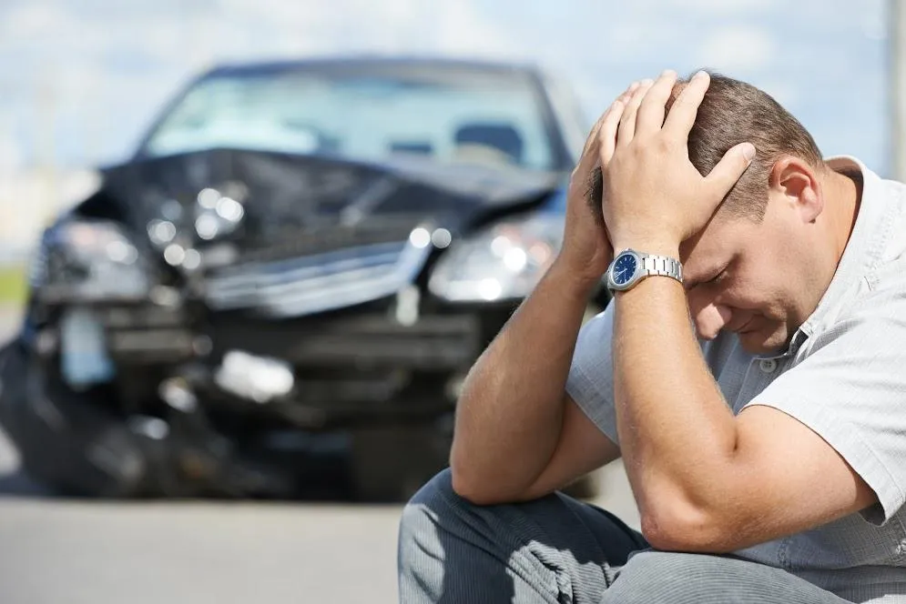 A man is kneeling down in front of a damaged car.