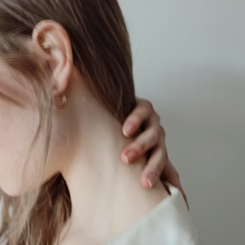 Hand touching the side of a person’s neck near the ear, against a plain light background