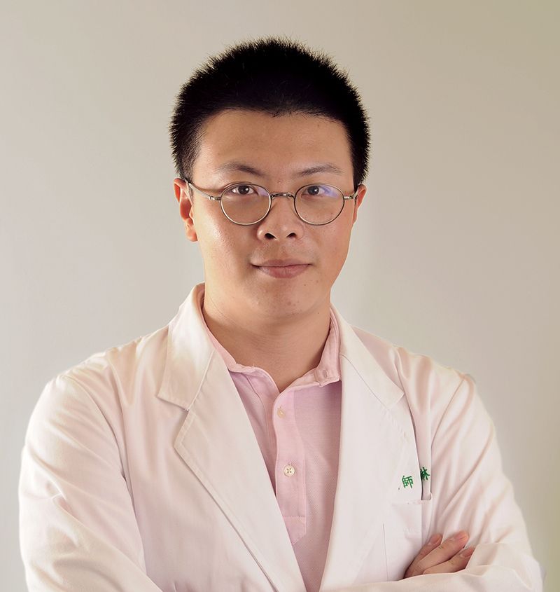 A man wearing glasses and a white coat stands with his arms crossed