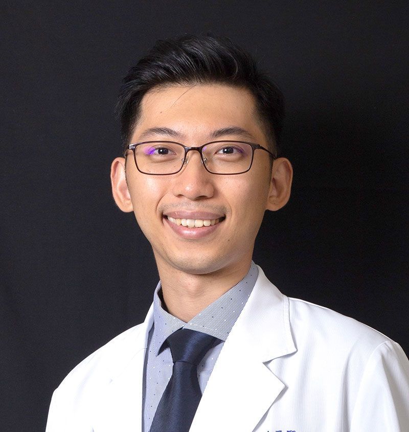 A young man wearing glasses and a white coat and tie is smiling for the camera.