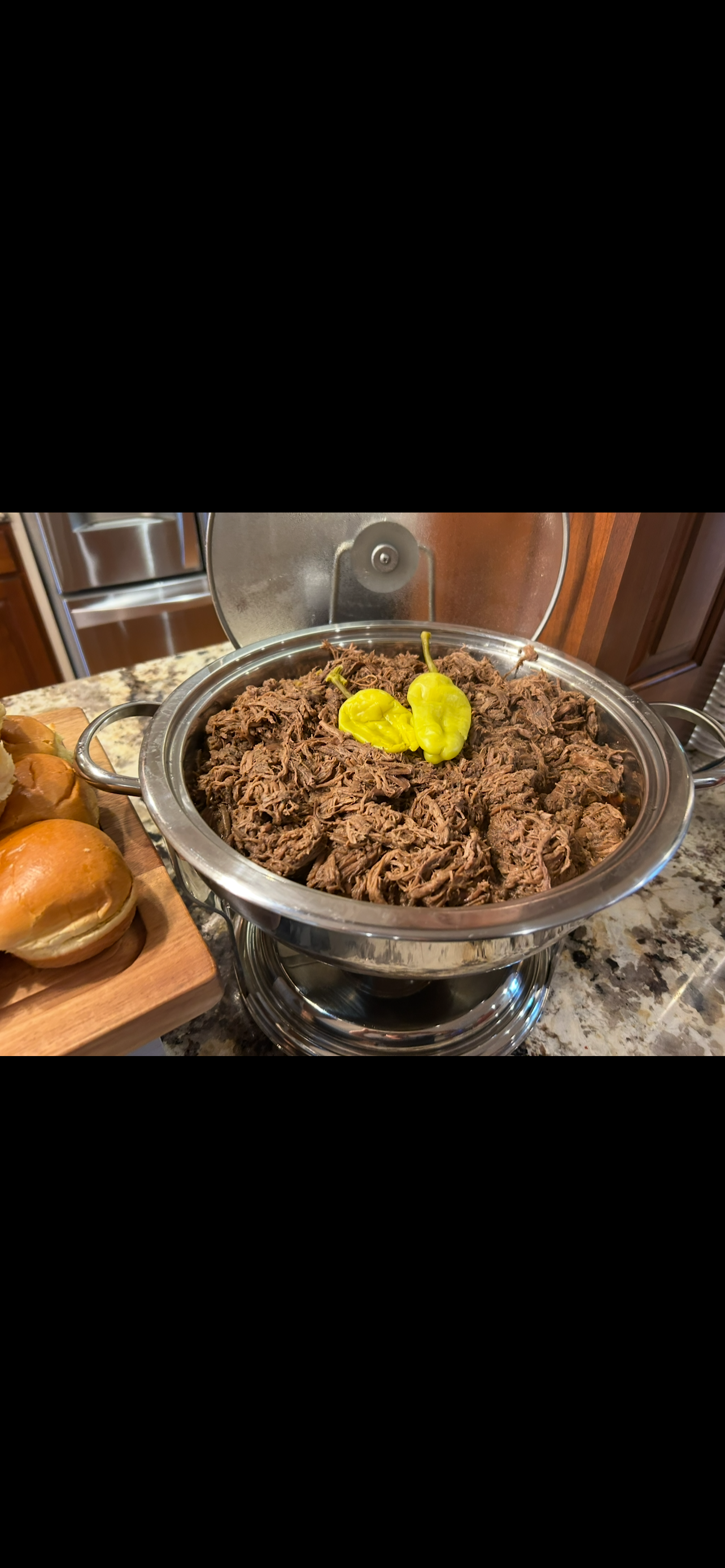 A bowl of cooked ground meat, topped with yellow peppers, sits on a countertop, with bread in the background.