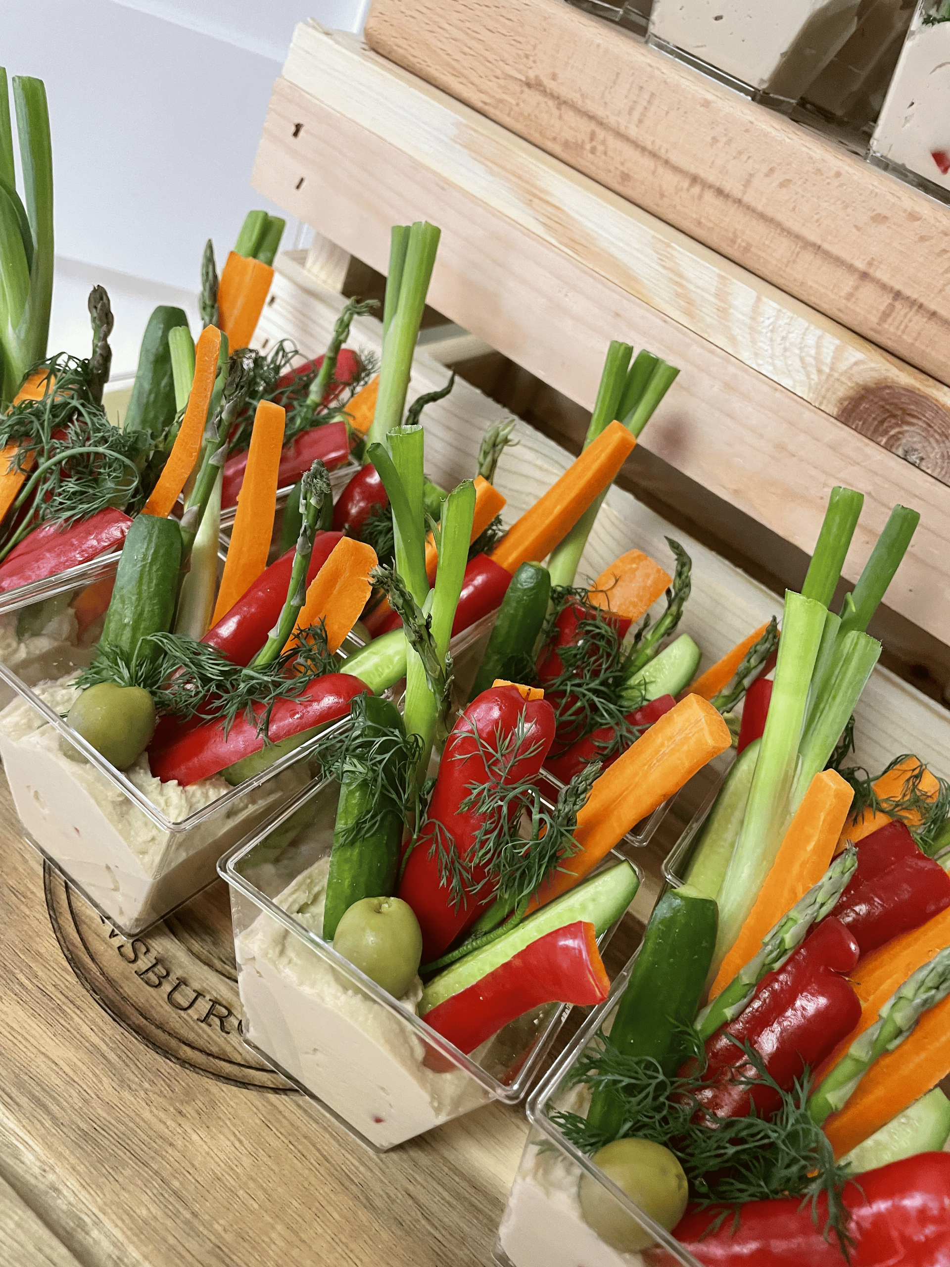 Vegetable crudités in clear cups with hummus; carrots, peppers, cucumbers, and green onions.