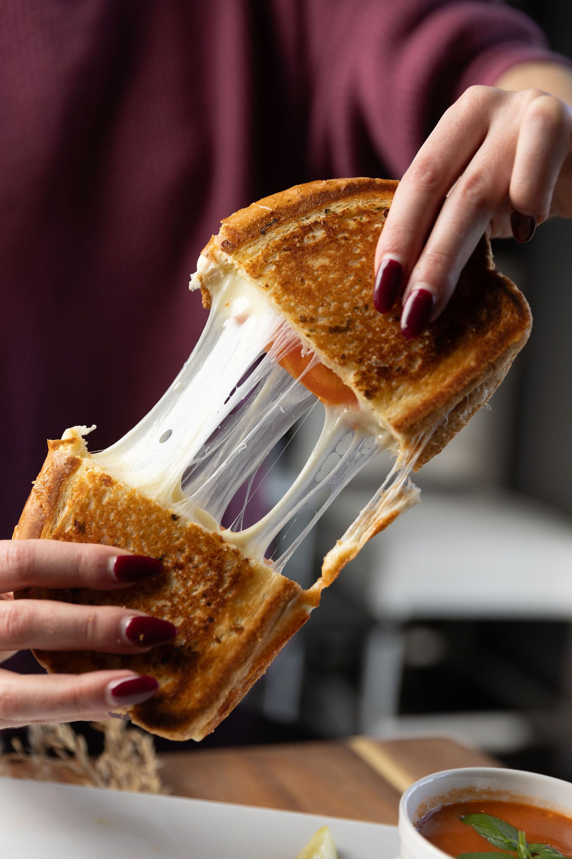 Person pulling apart a grilled cheese sandwich with gooey, melted cheese.