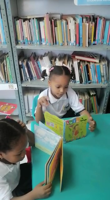 Two young girls are reading books in a library.