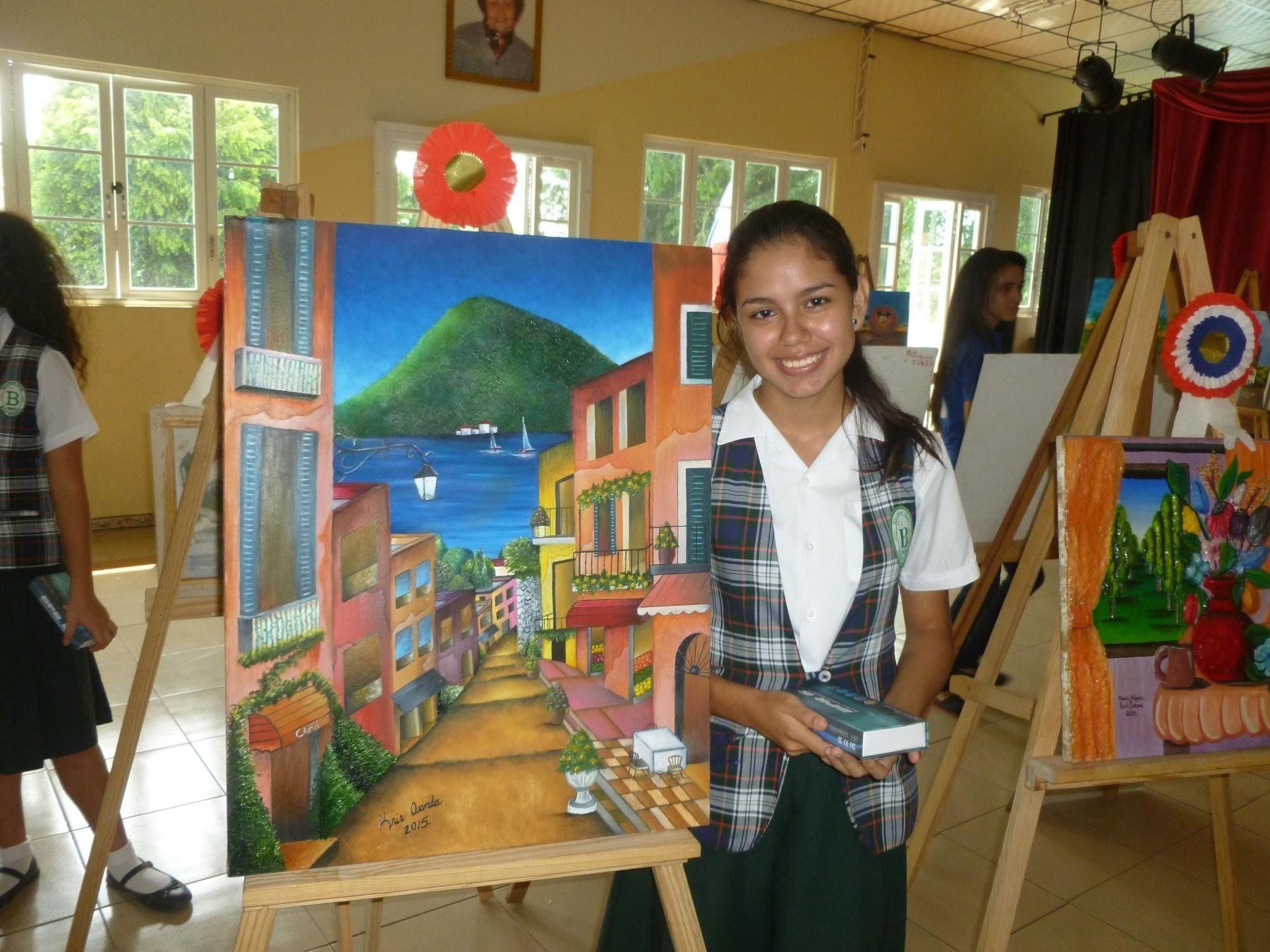 A girl is holding a book in front of a painting on an easel