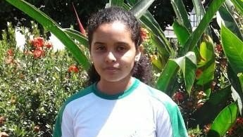 A young girl in a white and green shirt is standing in front of a bush.