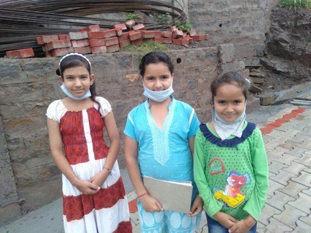 Three young girls wearing face masks are standing next to each other.