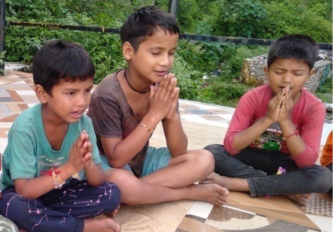 Three young boys are sitting on the floor with their hands folded in prayer.