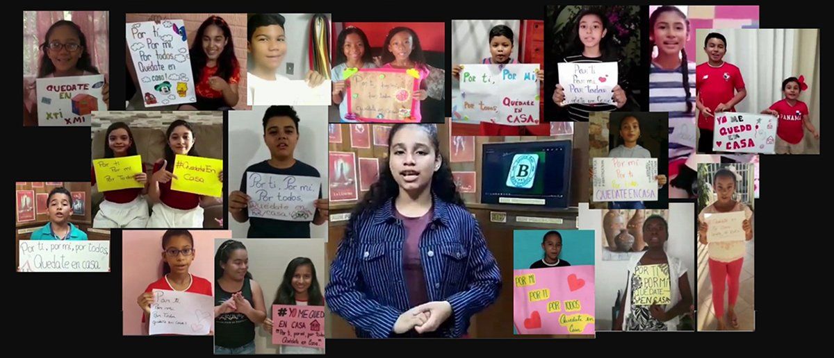 A girl is standing in front of a group of children holding signs.