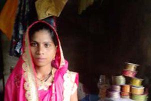 A woman in a pink sari is sitting in front of a pile of ribbons.
