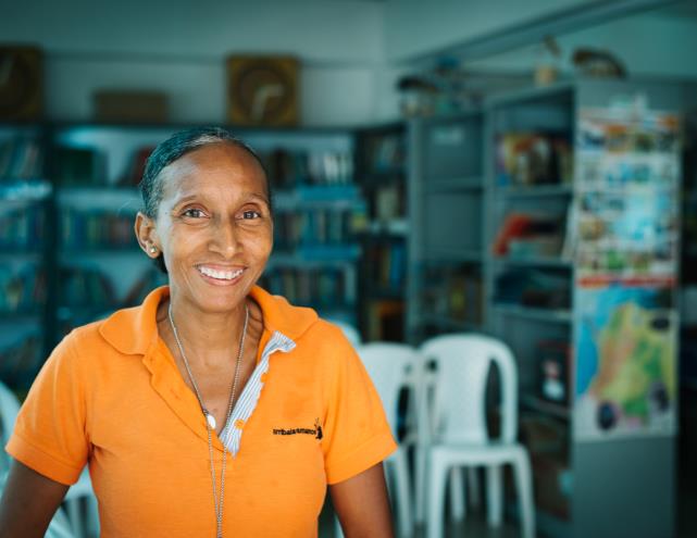 A woman in an orange shirt is smiling in a library.