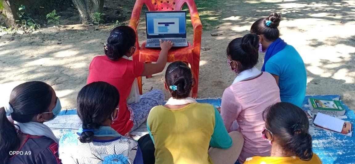 A group of people are sitting around a laptop computer.