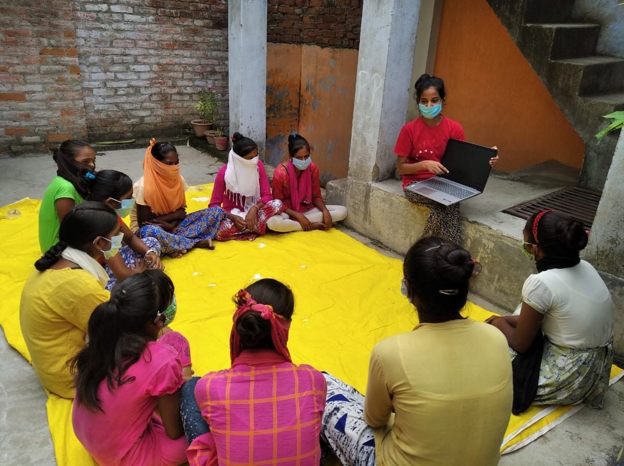 A group of women are sitting in a circle on a yellow tarp.