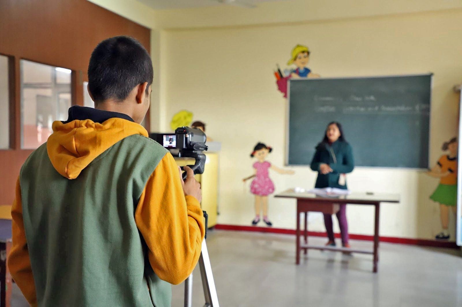 A boy is taking a picture of a woman in a classroom