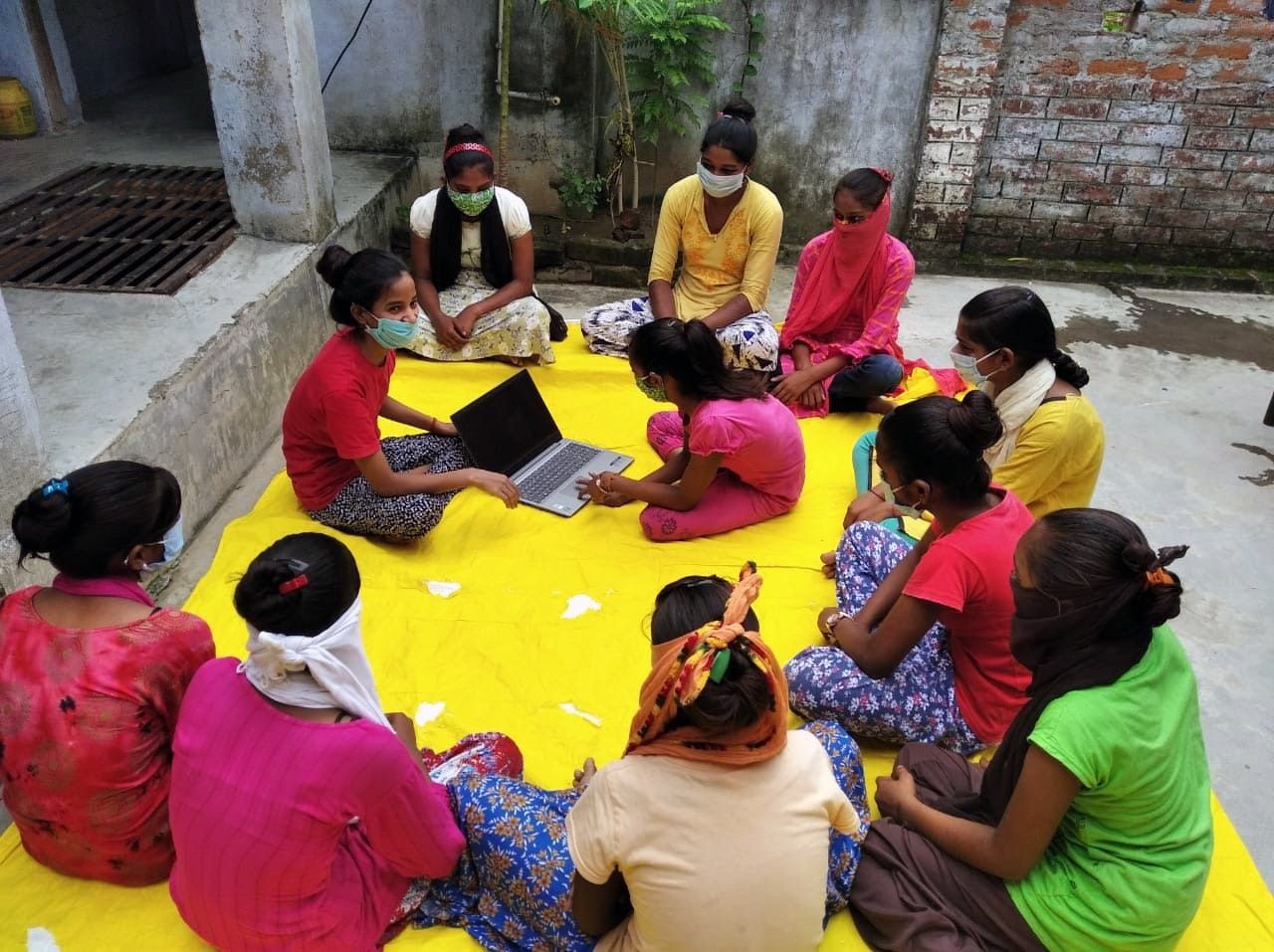 A group of people are sitting on a yellow blanket with a laptop.