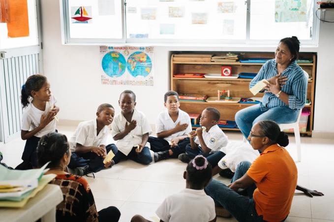 A group of children are sitting on the floor in a circle with a teacher.