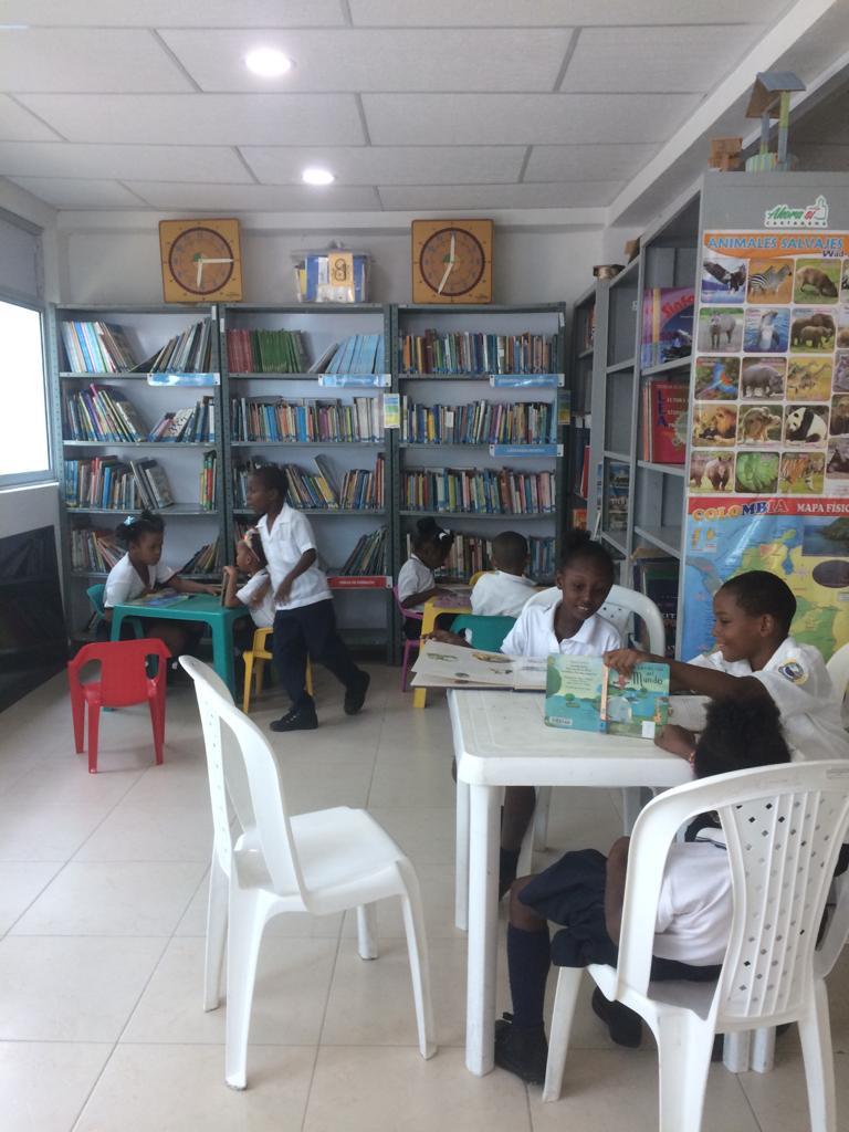 A group of children are sitting at tables in a library.