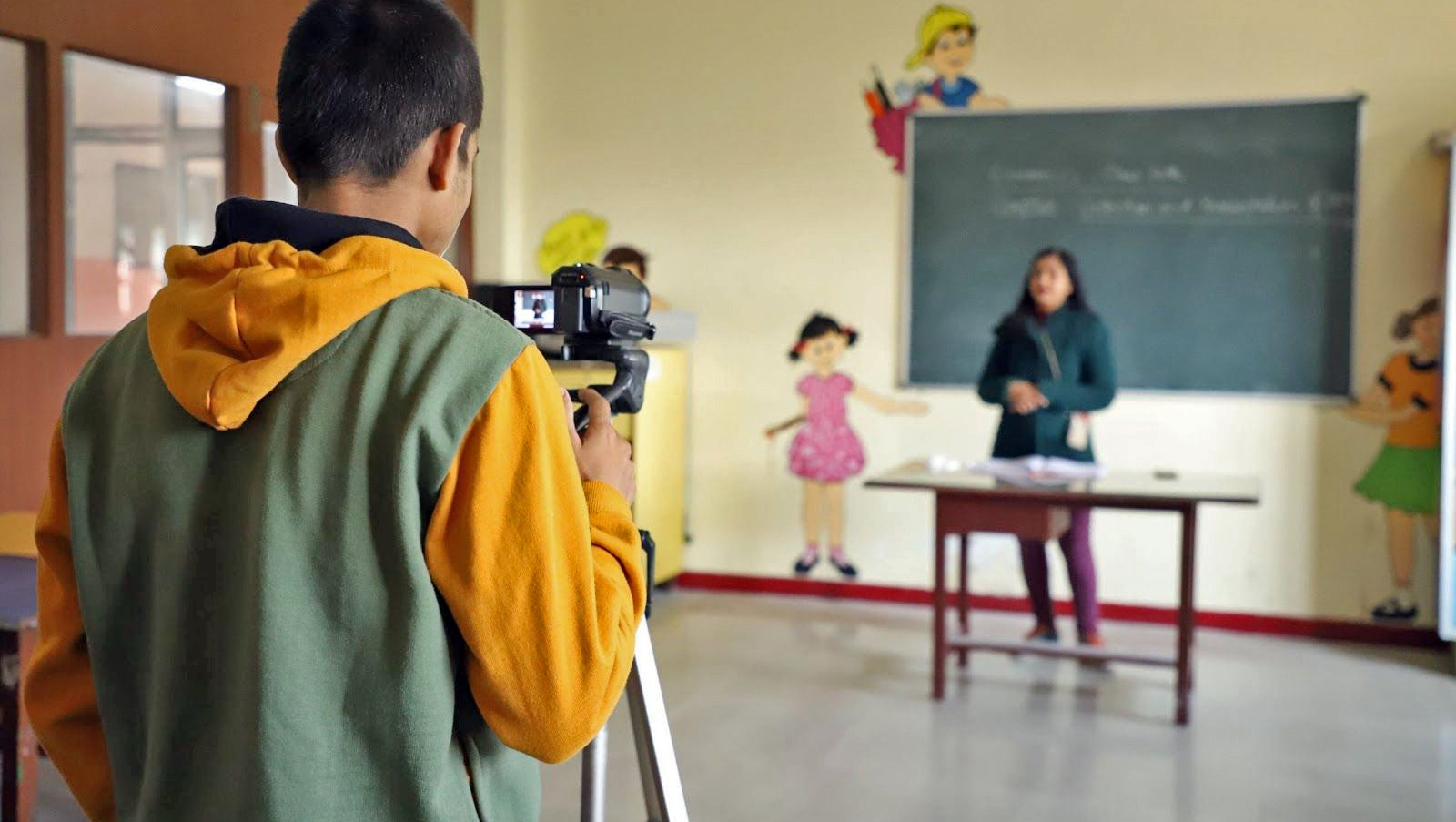 A man is taking a picture of a teacher in a classroom.