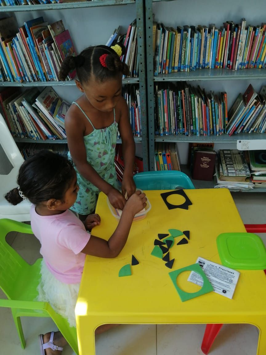 Two little girls are sitting at a yellow table in a library