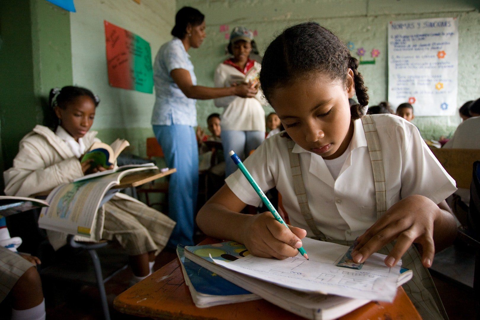 A girl is sitting at a desk in a classroom writing in a notebook.
