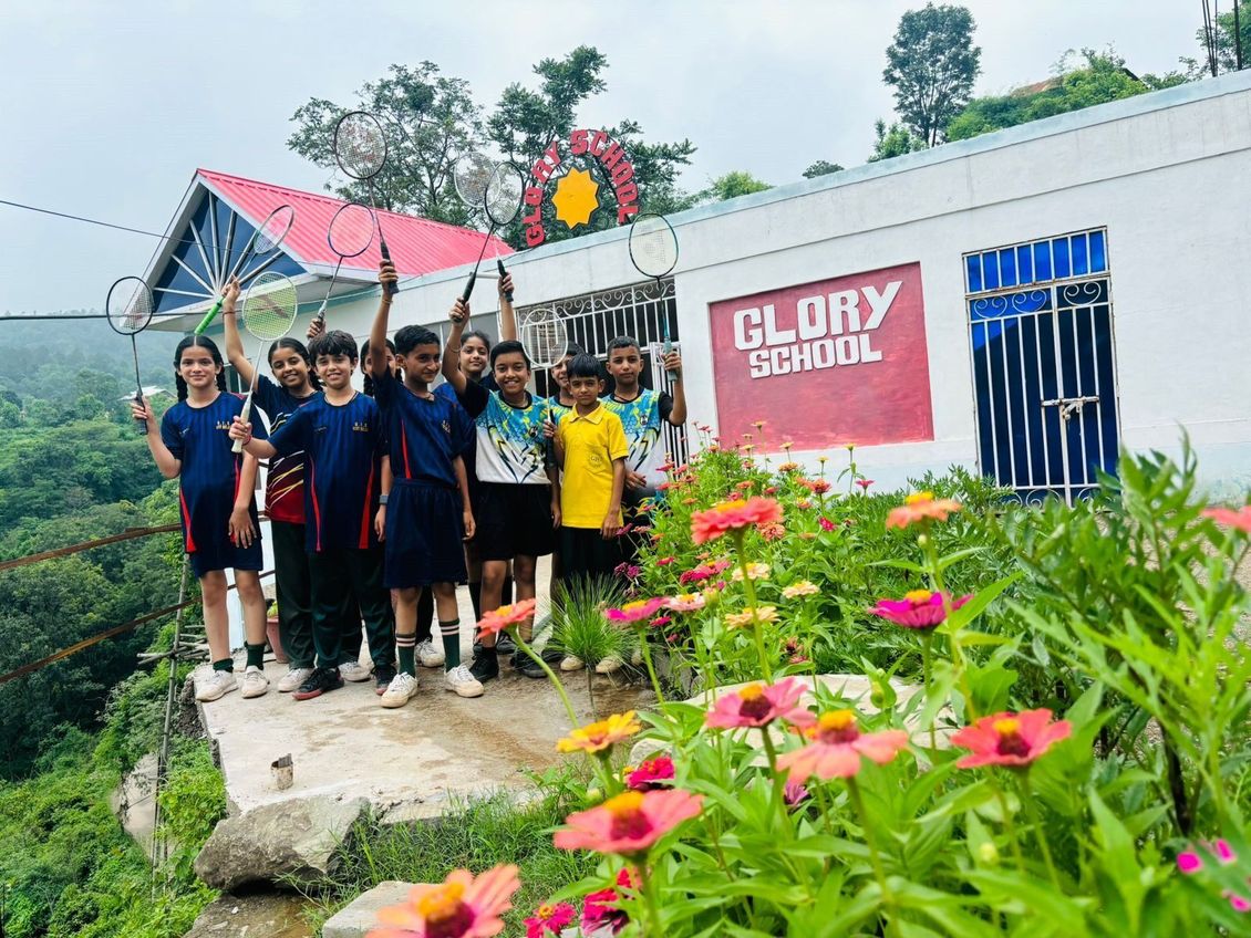 A group of children are standing in front of a building holding tennis rackets.