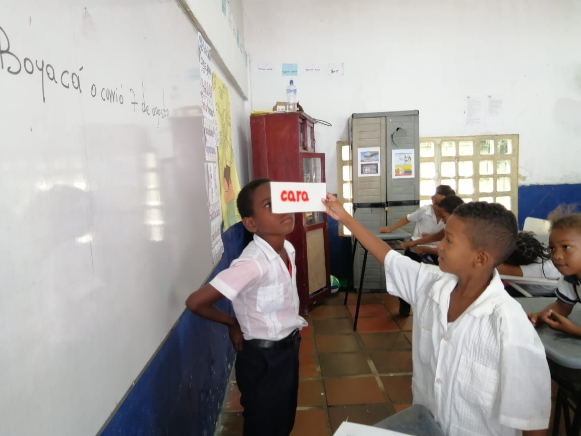 A boy in a classroom holds up a card that says oops