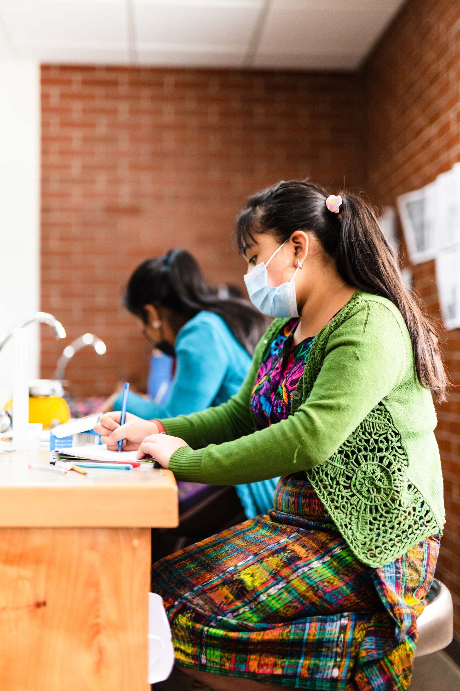 A woman wearing a mask is sitting at a desk.