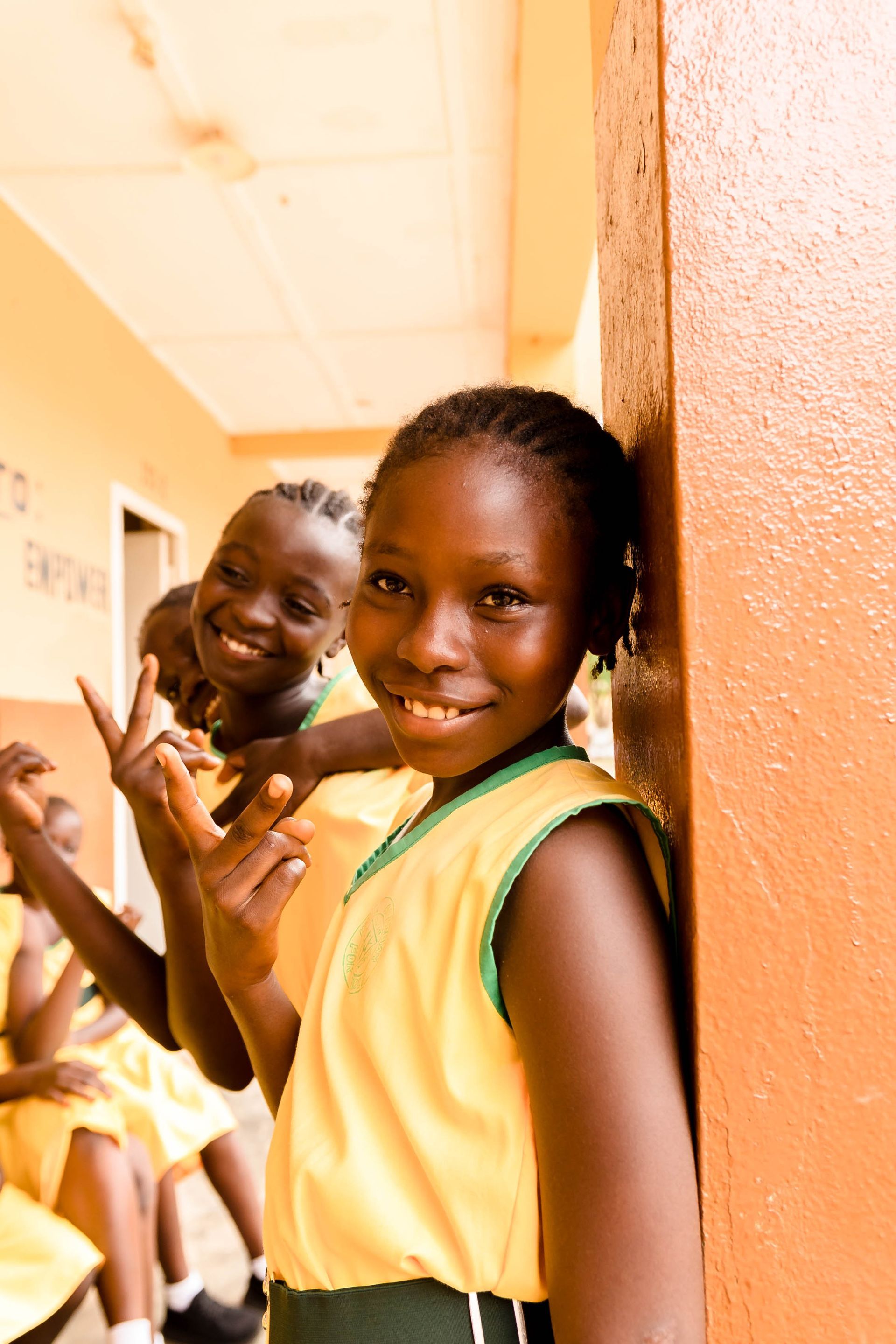 A girl in a yellow shirt is leaning against a wall and smiling.
