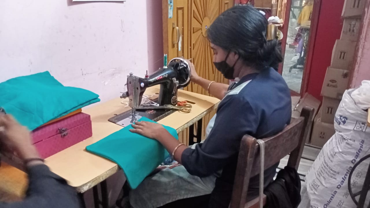 A woman wearing a mask is sitting at a table using a sewing machine.