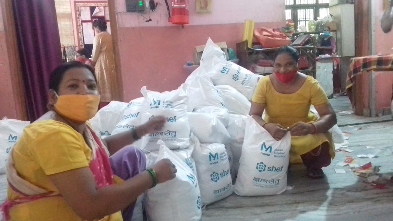 Two women wearing face masks are kneeling down in front of a pile of bags.