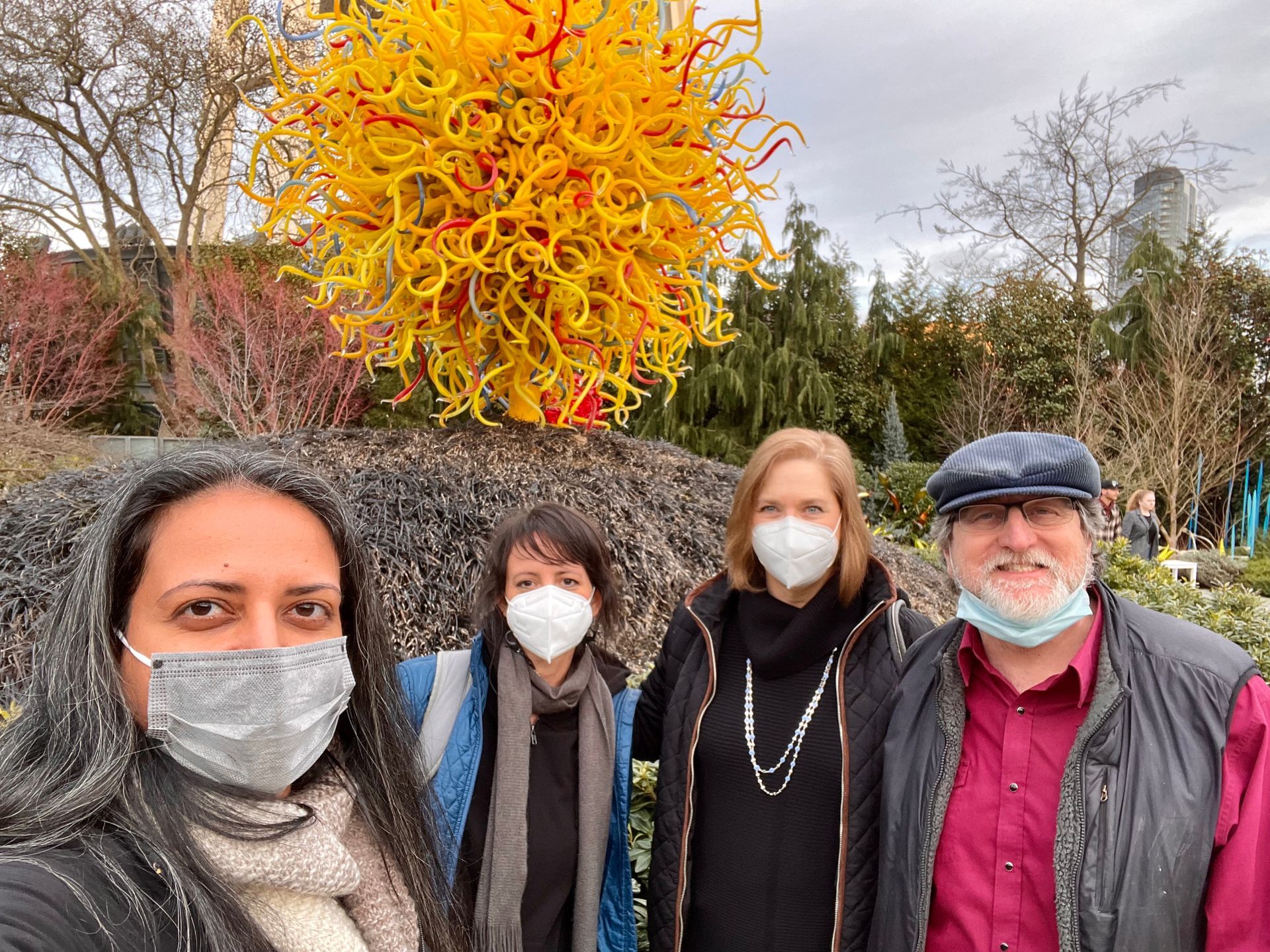 A group of people wearing face masks are standing in front of a sculpture.