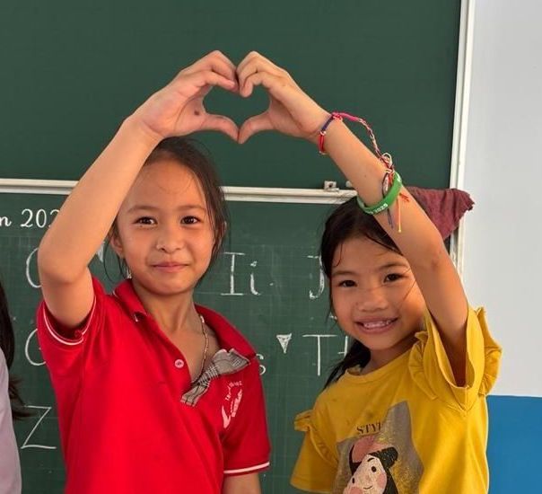 Two young girls are making a heart shape with their hands